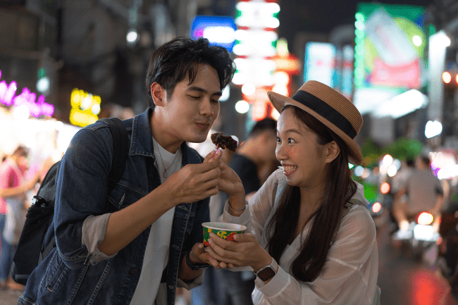 Pasangan pria dan wanita sedang menikmati makanan di tengah jalan raya saat malam hari